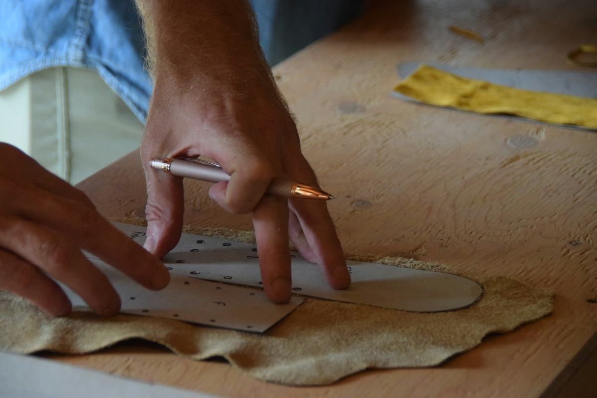 Hands tracing a pattern onto tan leather in a workshop